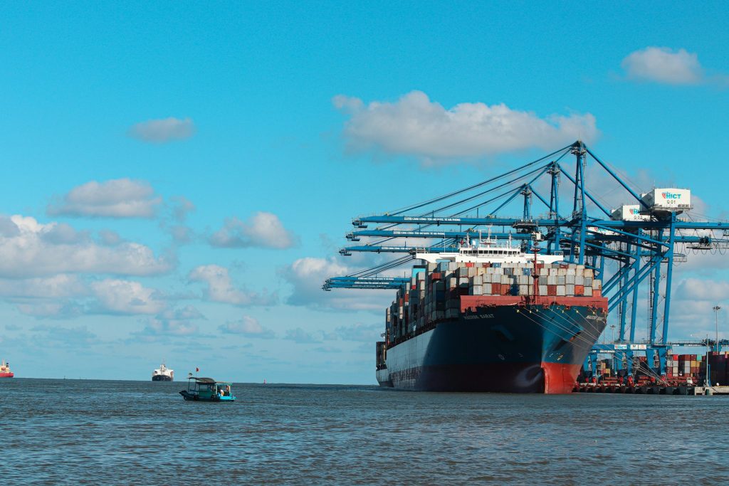 Container ship loading at a port with cranes against a blue sky